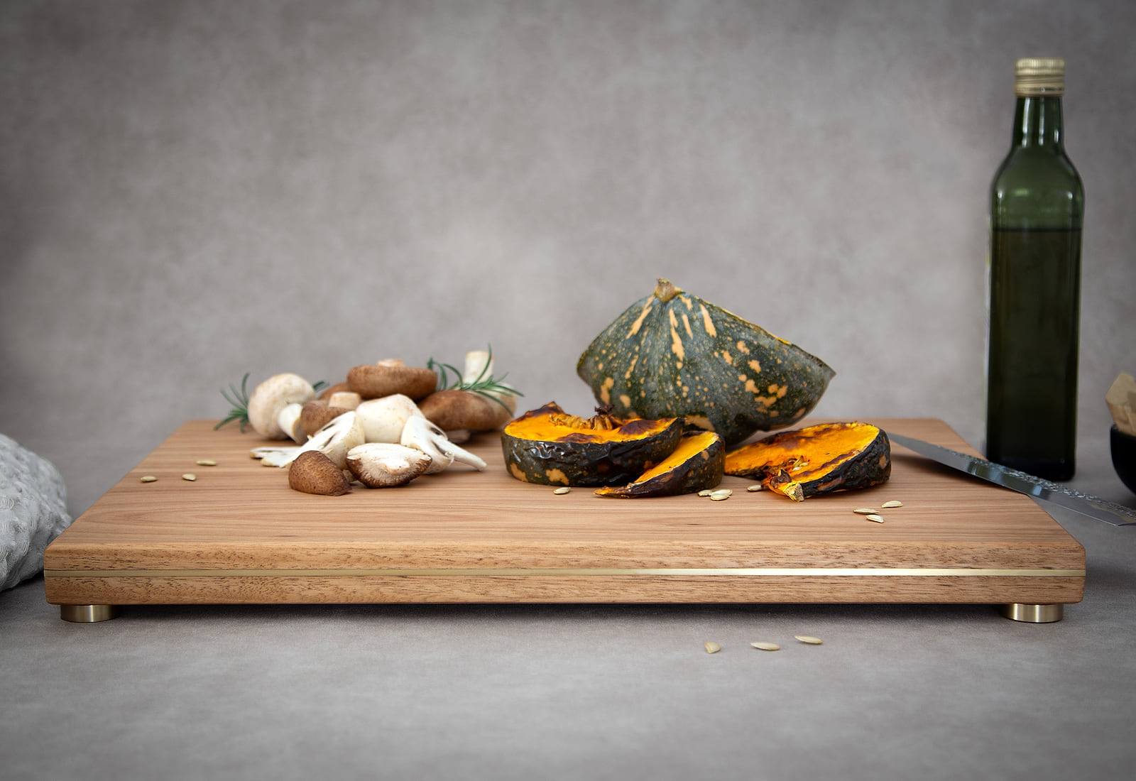 A HEWN chopping and serving board in Blackbutt, brass inlaid along its edge and raised on brass feet, with roast pumpkin, mushrooms and rosemary